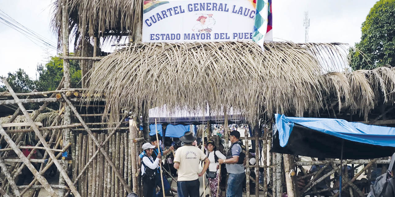 Hombres con chalecos negros y palos vigilan el “Cuartel General de Lauca Ñ”,  Cochabamba. 