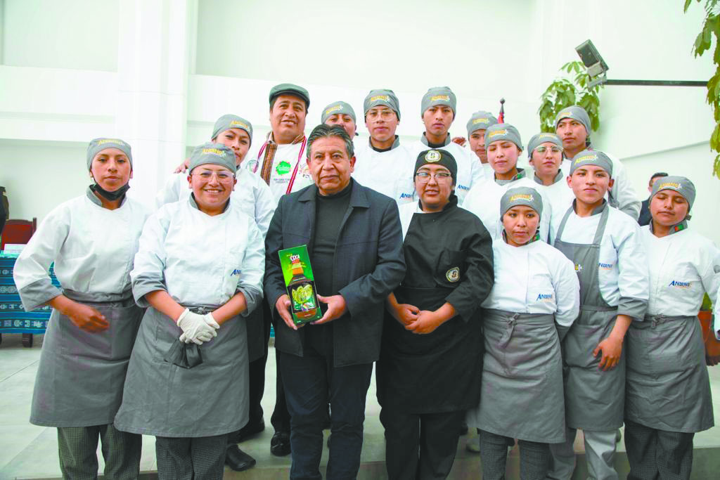 El Vicepresidente posa con alumnos de Gastronomía y lleva en las manos un licor de coca.