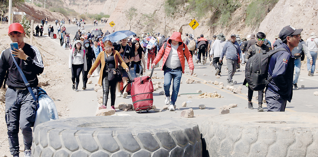 Decenas de personas caminan en medio de piedras y llantas en una vía de Cochabamba. Foto:  APG